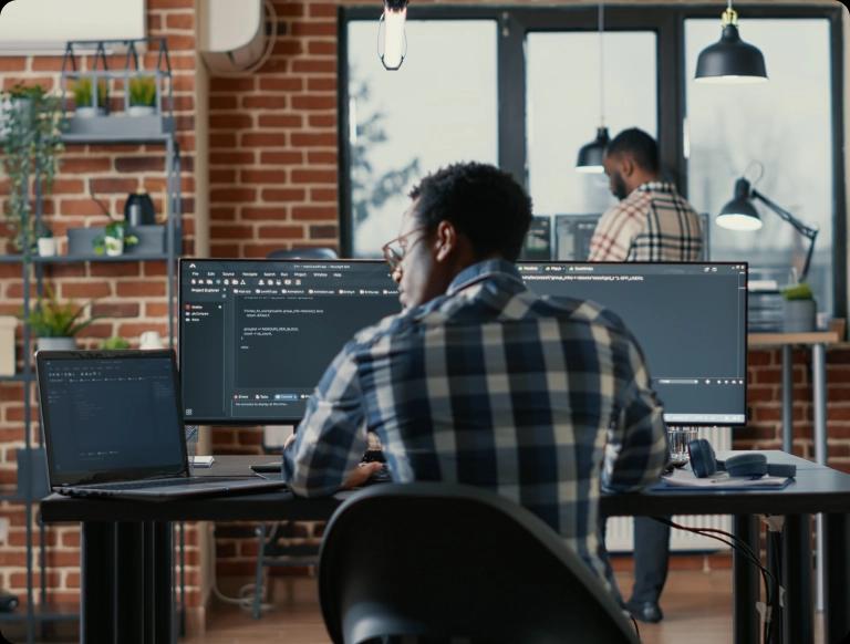 A Black man with glasses and curly hair working on a computer monitor developing applications and software.